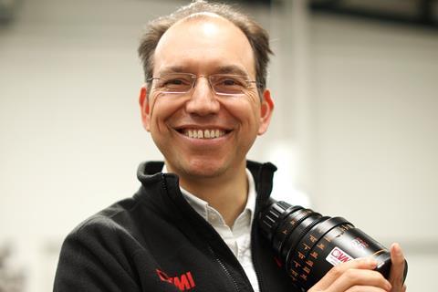 Headshot of man with glasses holding camera lens